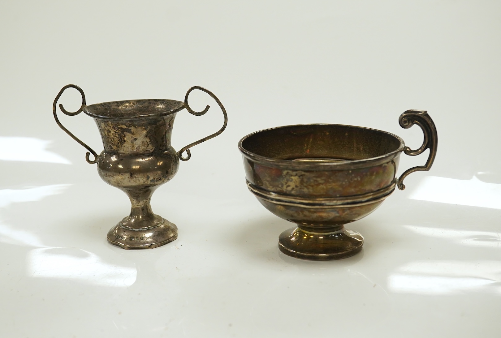 A William IV silver christening mug, London 1834, 10cm, a George III silver cream jug, London, 1799 and three small silver trophy cups. Condition - poor to fair